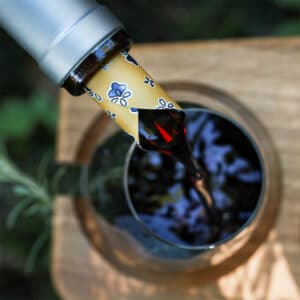 Vin rouge versé proprement dans un verre grâce à un DropStop® décoré de motifs floraux inséré dans le goulot de la bouteille.